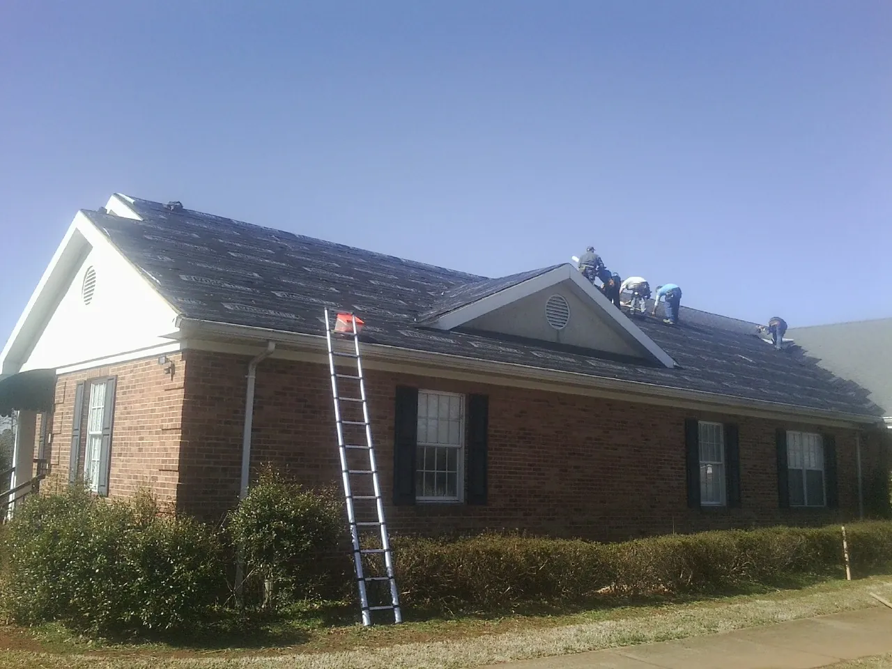 Crew tearing shingles off a brick ranch roof with a ladder set — Metal Roof Repair work by our crew in Durham